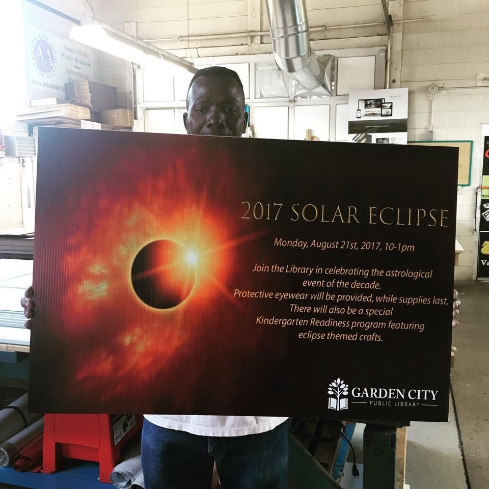 A person holds a large sign announcing a 2017 solar eclipse event at the Garden City Public Library.