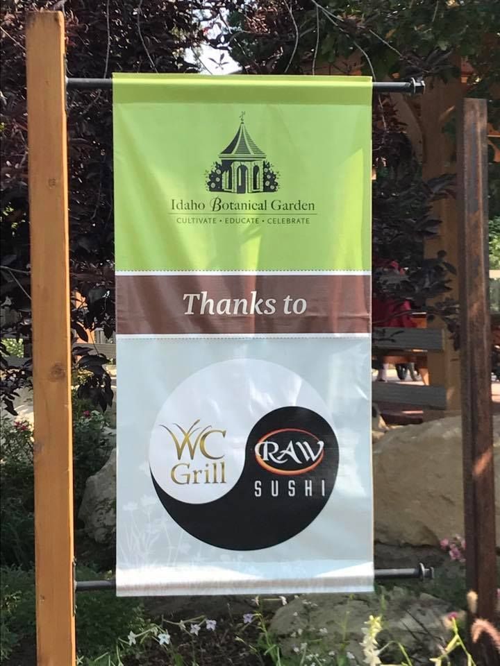 A hanging sign at the Idaho Botanical Garden thanking WC Grill and Raw Sushi, featuring their yin-yang style logo.