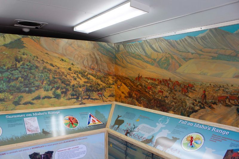 An educational exhibit featuring a wall-sized mural of a mountainous landscape with text and diagrams about wildlife.
