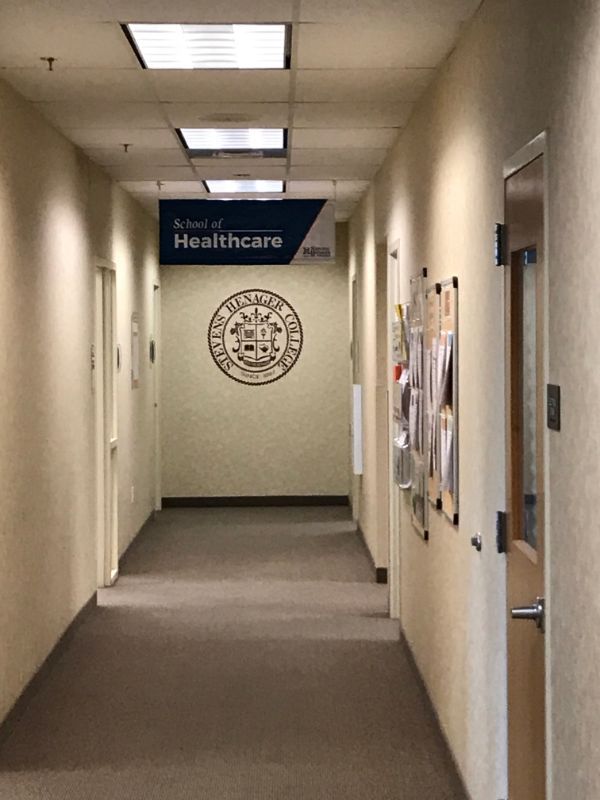 A hallway with a ceiling sign for the School of Healthcare and a college seal on the far wall.