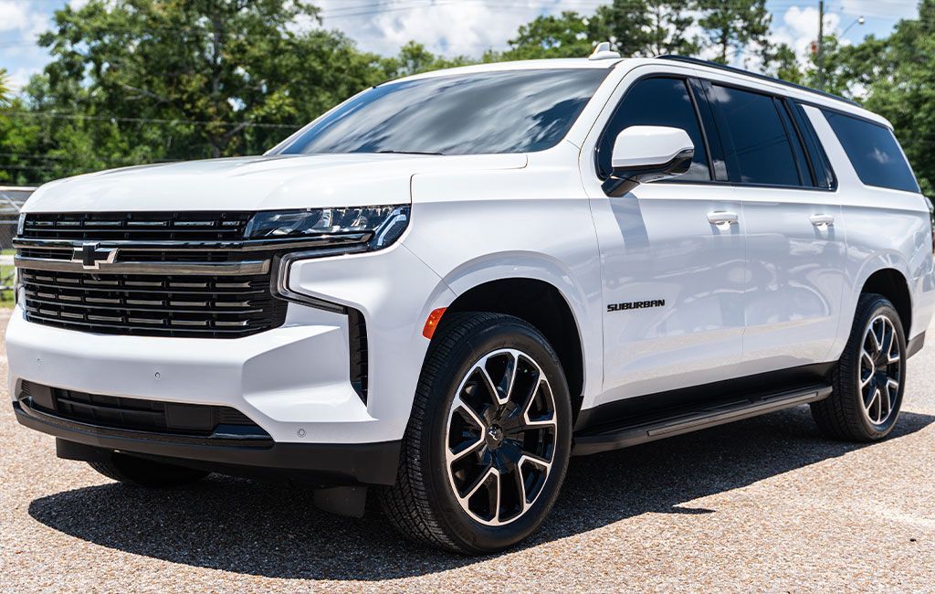 A white chevrolet suburban suv is parked in a gravel lot.