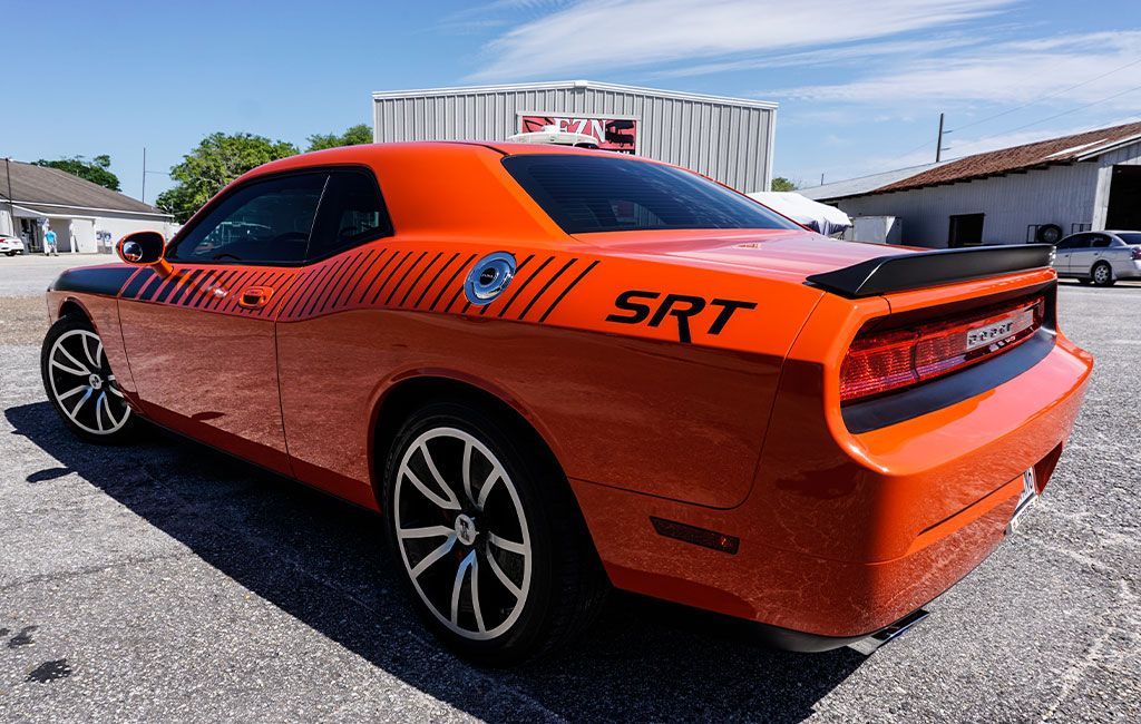 An orange dodge challenger srt is parked in a gravel lot.