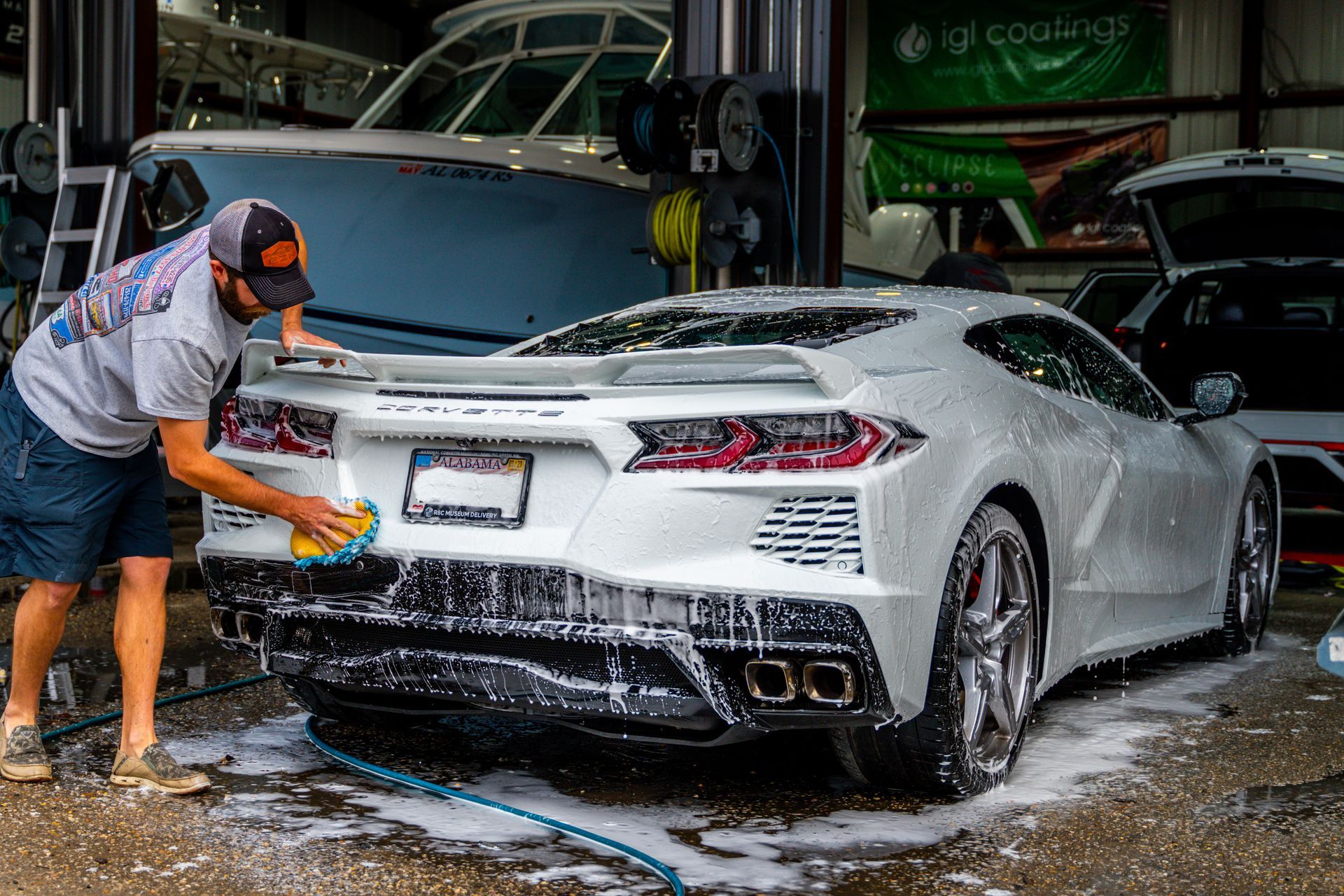 A man is washing a white sports car in a garage.
