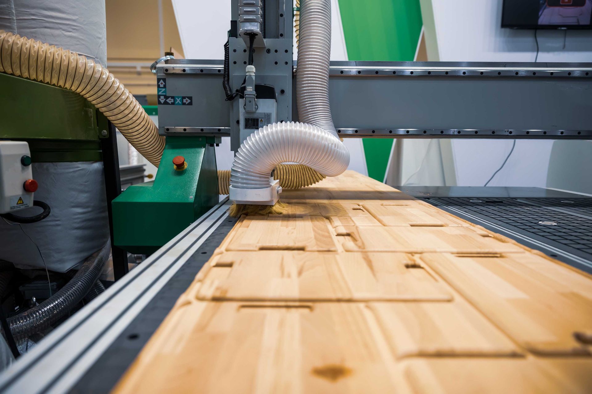 Gros plan d'une machine CNC découpant du bois. Bois clair découpé, machine en métal, panneau de commande vert et tuyau.