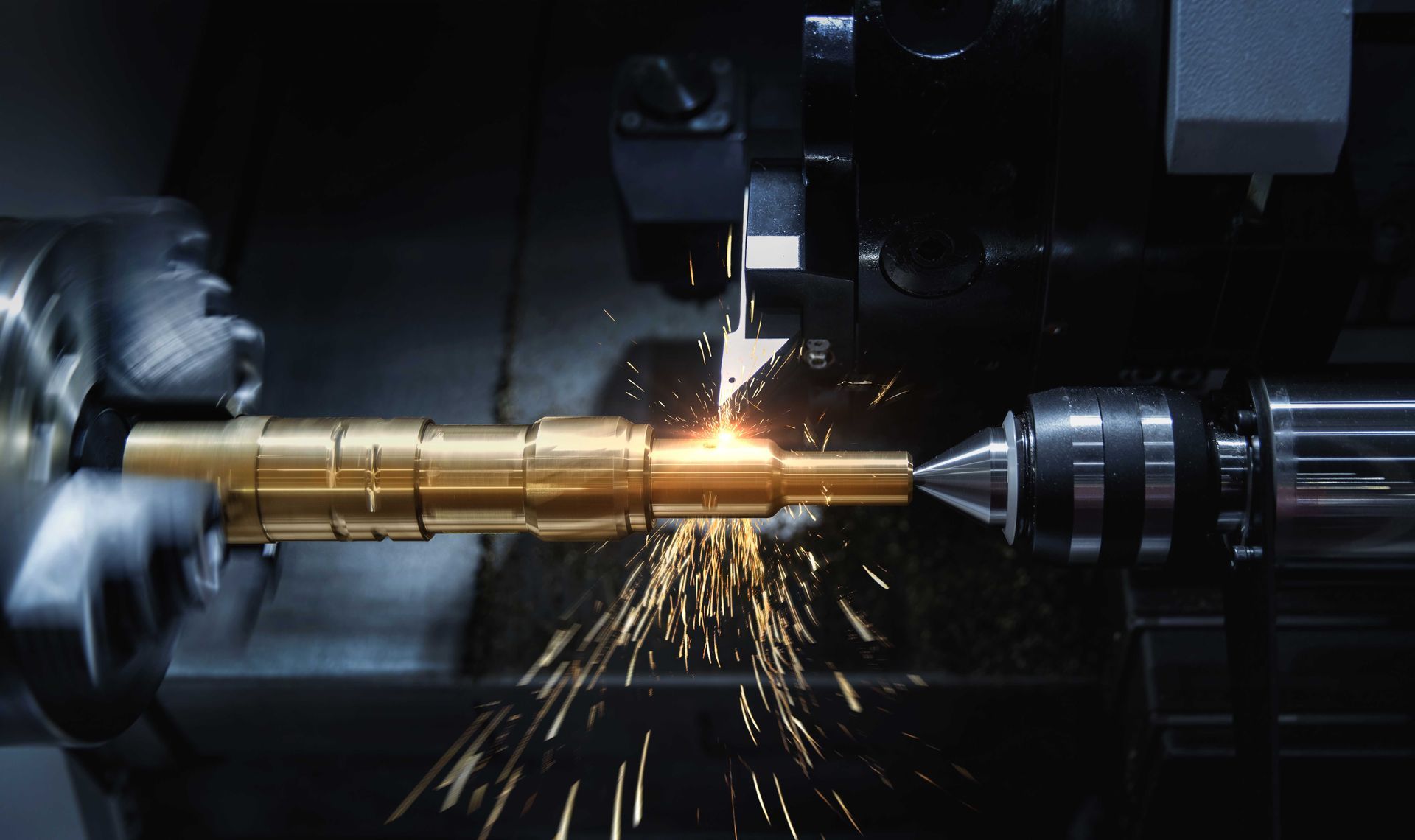 Un tour à métaux en train de couper une tige de laiton, des étincelles jaillissant dans un atelier faiblement éclairé.