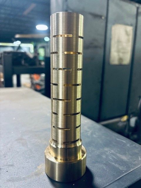 Une pièce cylindrique en laiton comportant des fentes horizontales repose sur une surface métallique dans un atelier.