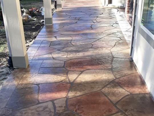 A concrete walkway leading to a house with a stone pattern.