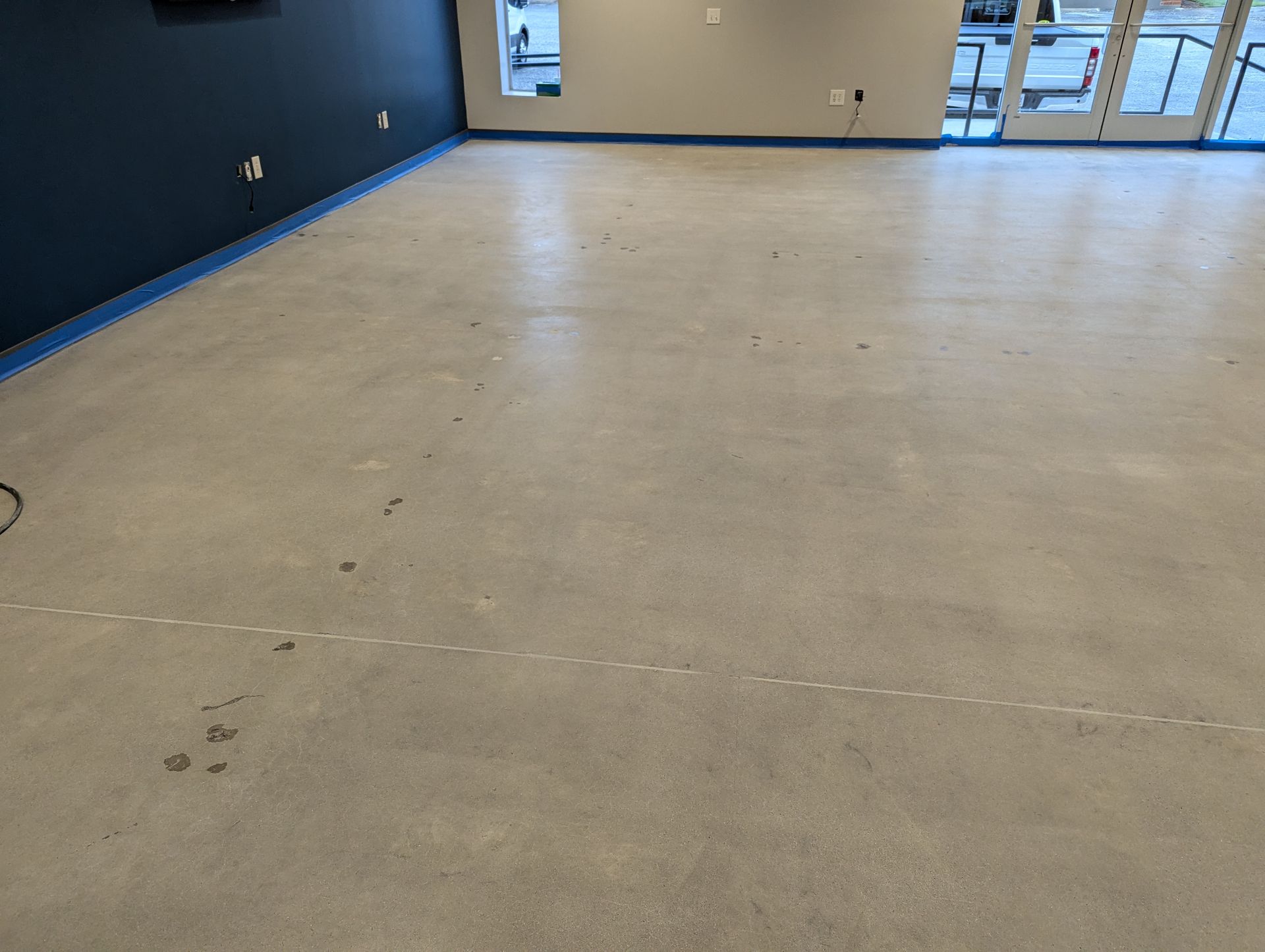 A large empty room with a concrete floor and blue tape on the floor.