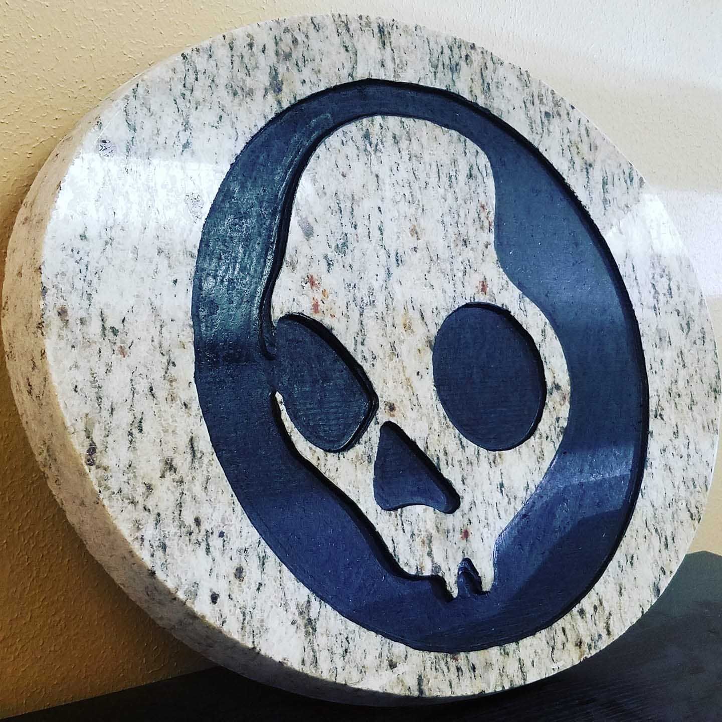 A skull in a blue circle is carved into a stone