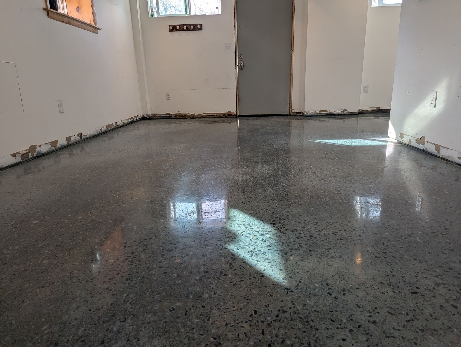 Empty room with glossy speckled floor and light reflecting from windows and doors