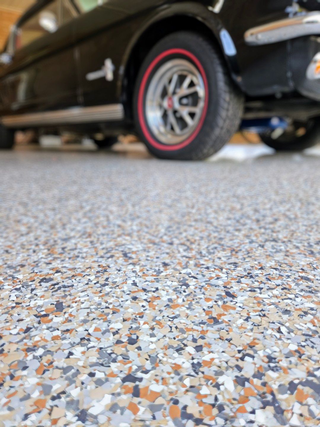 A black car is parked in a garage with a colorful floor.
