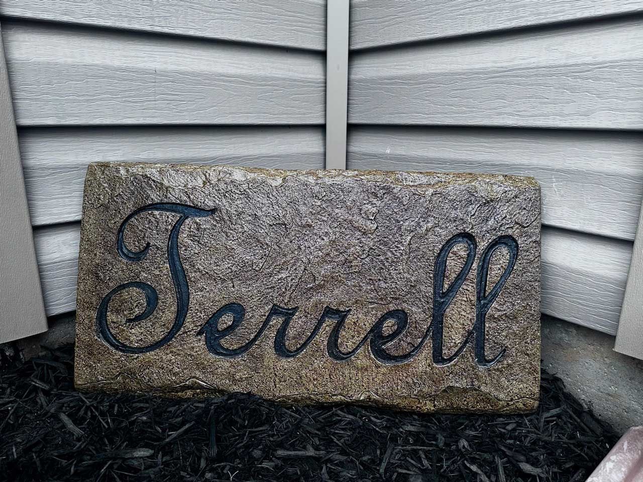 A stone with the name terrell carved into it is sitting in front of a house.