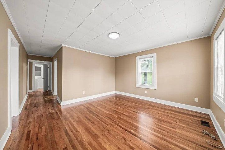 Empty living room with hardwood floors, beige walls, white trim, and a single window.
