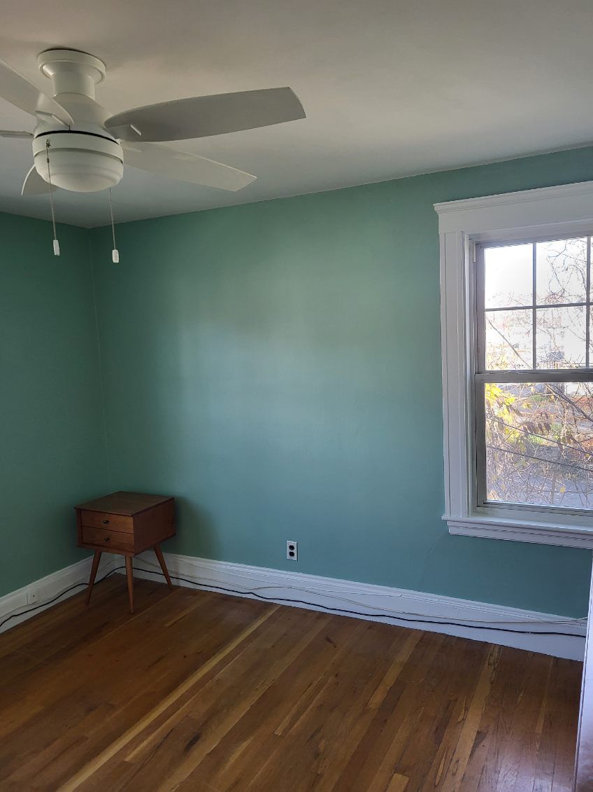 Empty mint-green bedroom with hardwood floor, white ceiling fan, and a window with white trim.