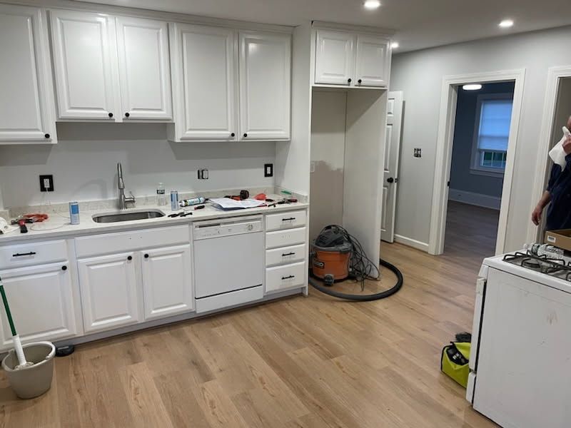 Bright kitchen with white cabinets, wood floors, and a vacuum hose near an open doorway