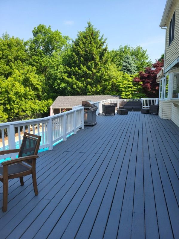 Spacious gray deck with white railing, chairs, and grill overlooking a green backyard and trees