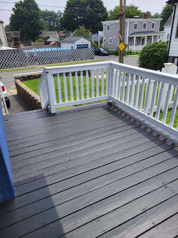 Gray deck with white railing overlooking a residential street and houses