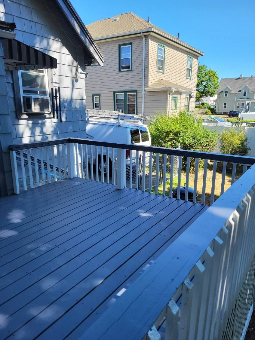 Blue wooden deck with white railings beside a house, overlooking a neighborhood backyard.