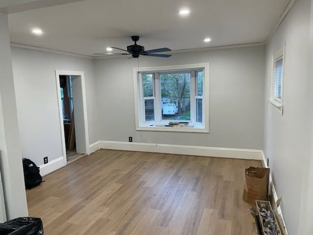 Empty gray living room with hardwood floor, ceiling fan, and large front window.