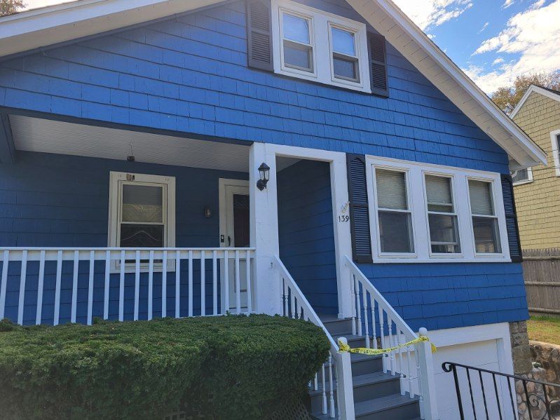 Blue house with white trim, front porch, and stairs in a sunny residential neighborhood