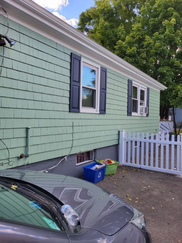 Light green house exterior with black shutters, white picket gate, and a parked gray car in front