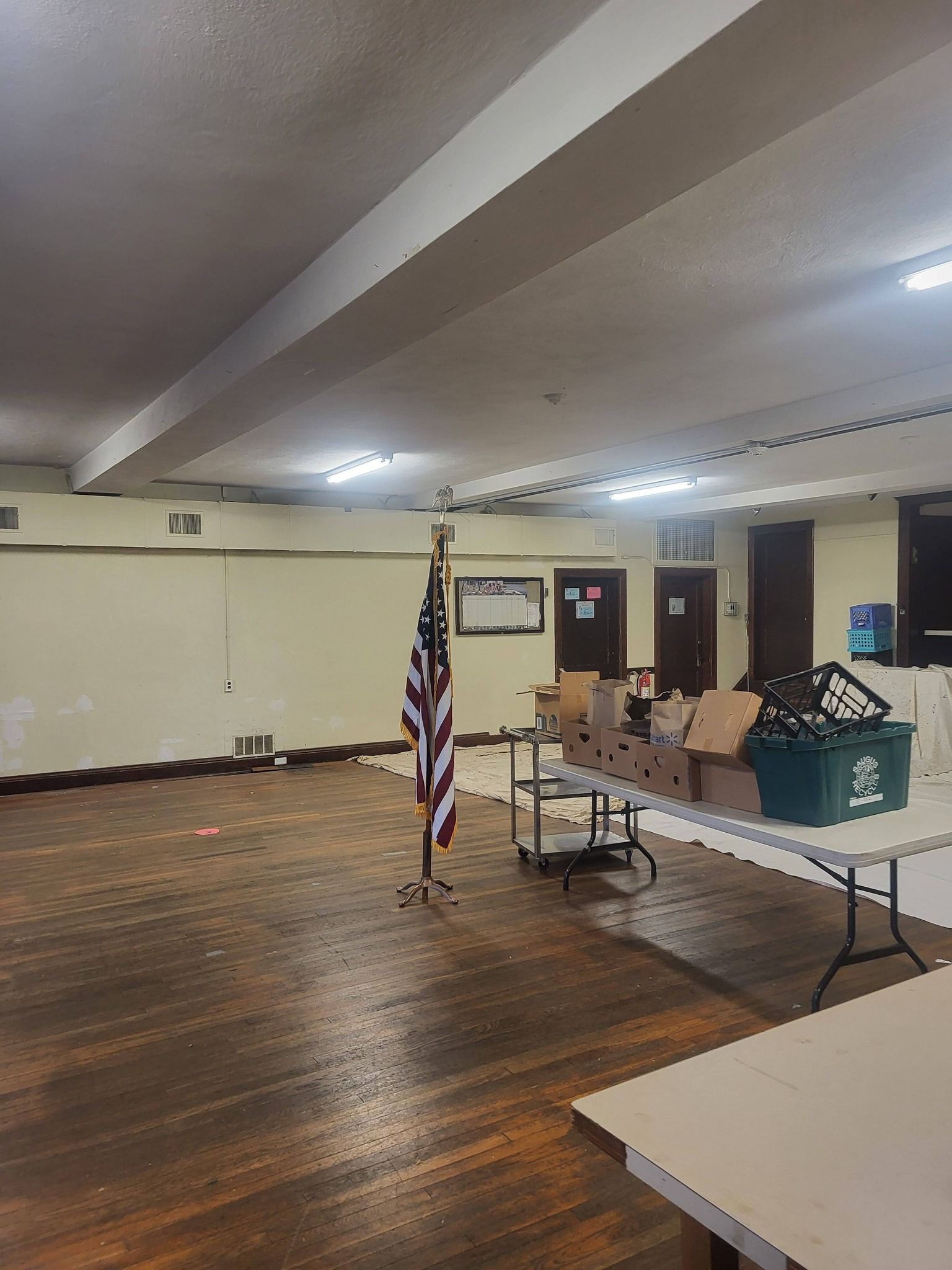 Empty community room with folding tables, chairs, American flag, and a small stage area