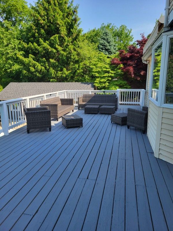 Spacious gray deck with wicker patio furniture, white railing, and green trees in the background
