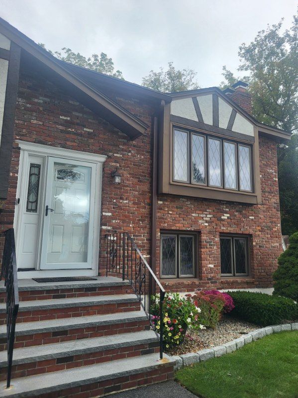 Brick house front with steps, white door, and large Tudor-style windows under a cloudy sky