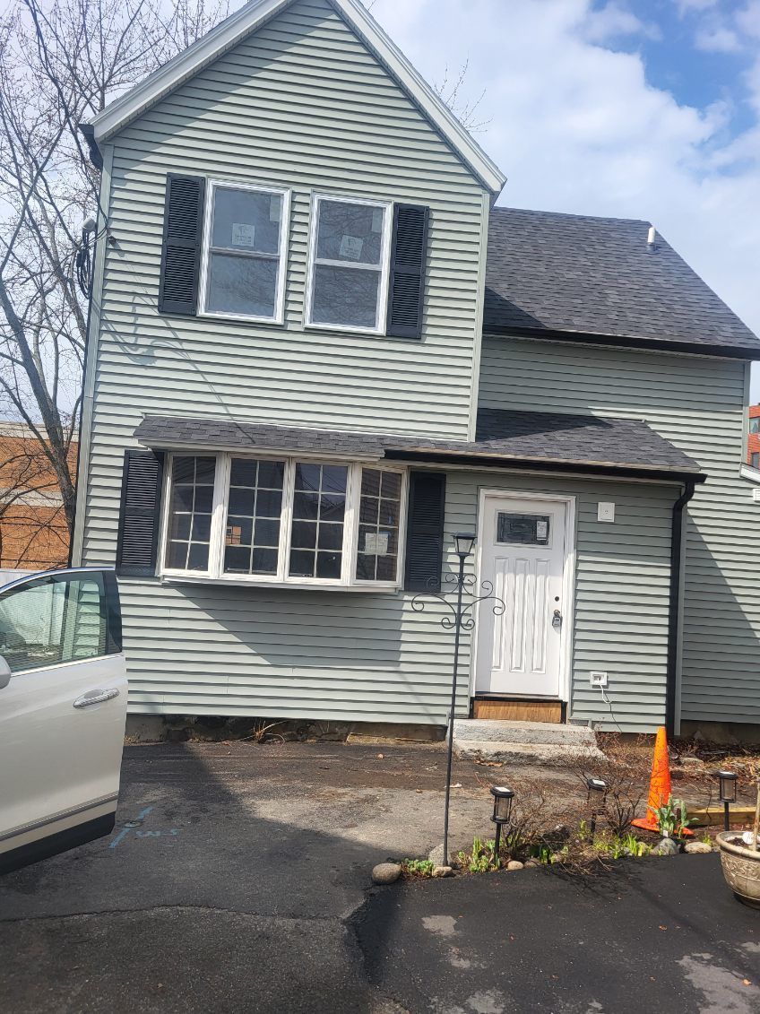 Gray two-story house with white trim, black shutters, small porch, and driveway