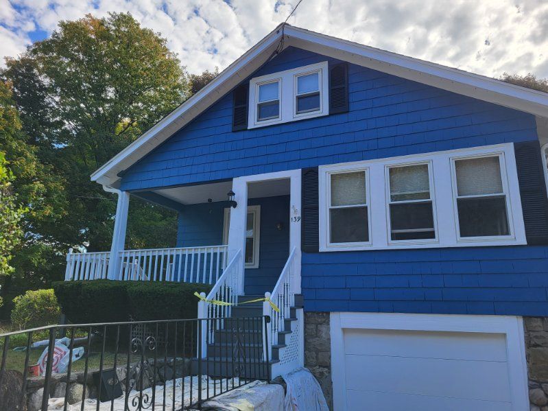 Blue house with white trim, front porch, and garage beneath a bright sky