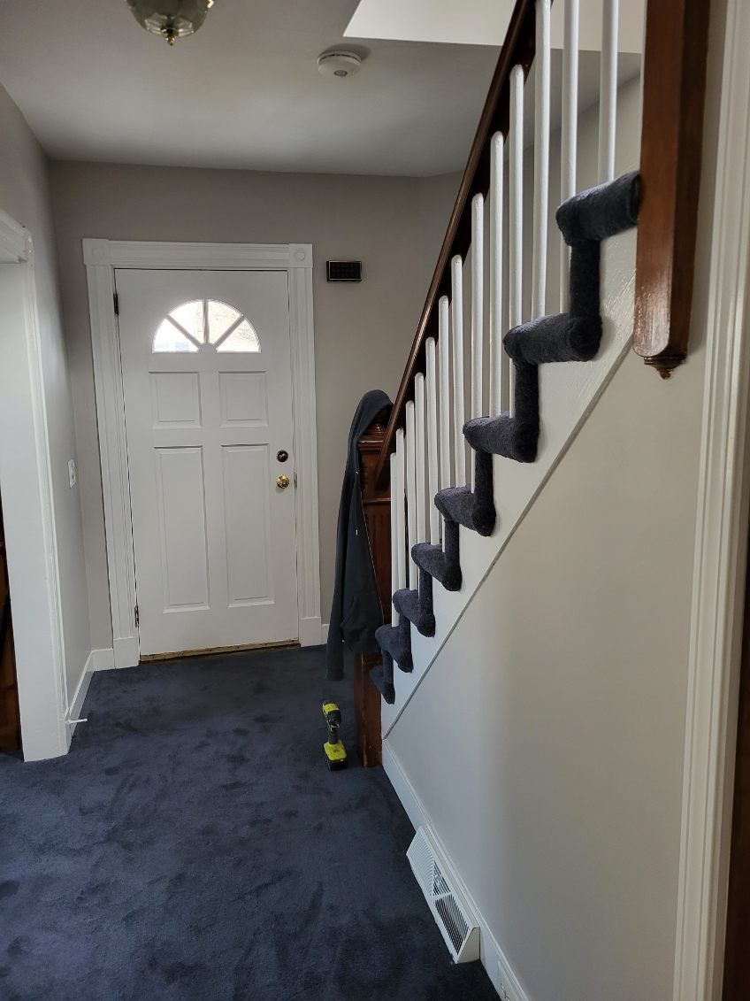 Narrow hallway with a white front door and staircase with black carpet runners on the right.