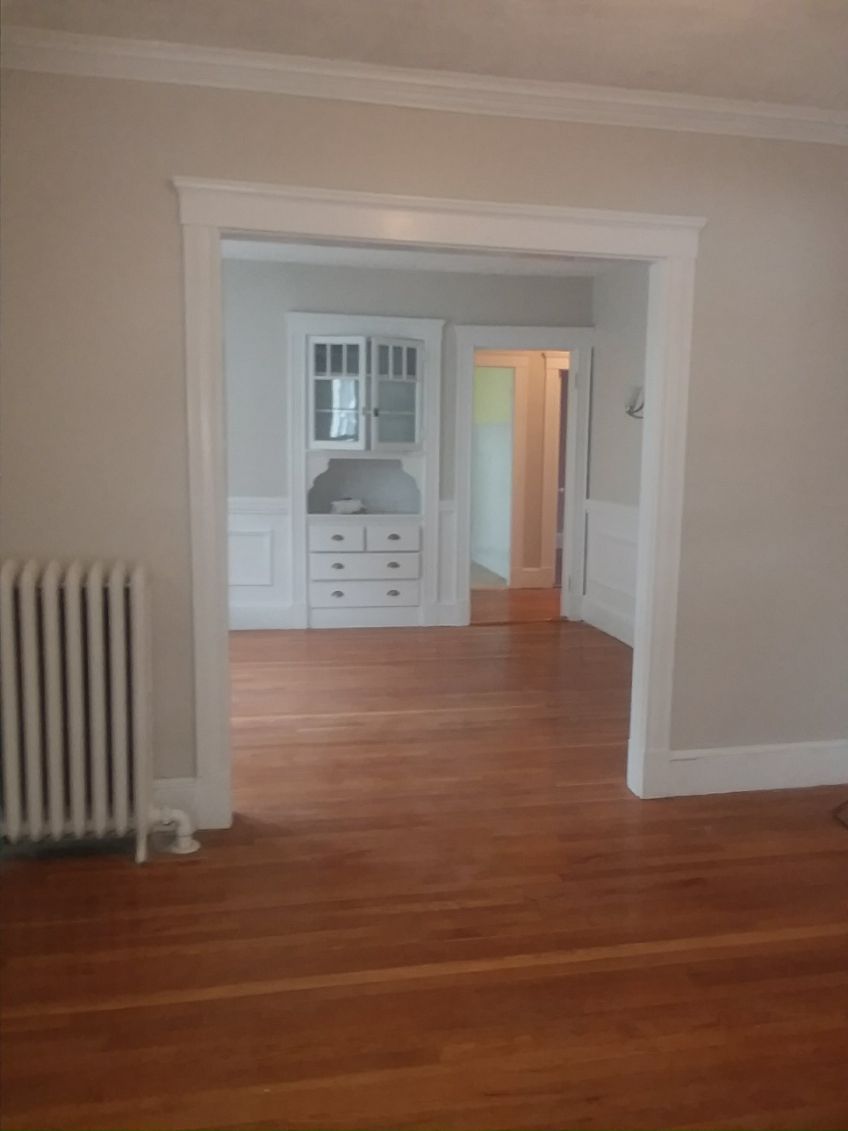 Empty room with hardwood floors, a white radiator, and a doorway to a built-in cabinet area.