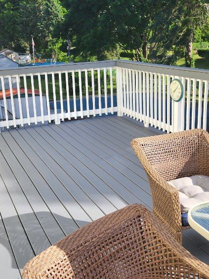 Patio deck with white railing, gray floorboards, wicker chairs, and trees in the background