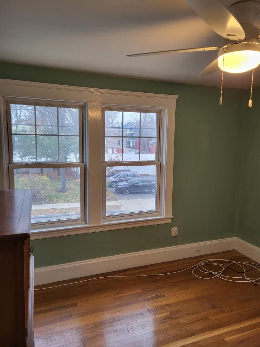 Empty room with green walls, hardwood floor, large window, and ceiling fan with light.