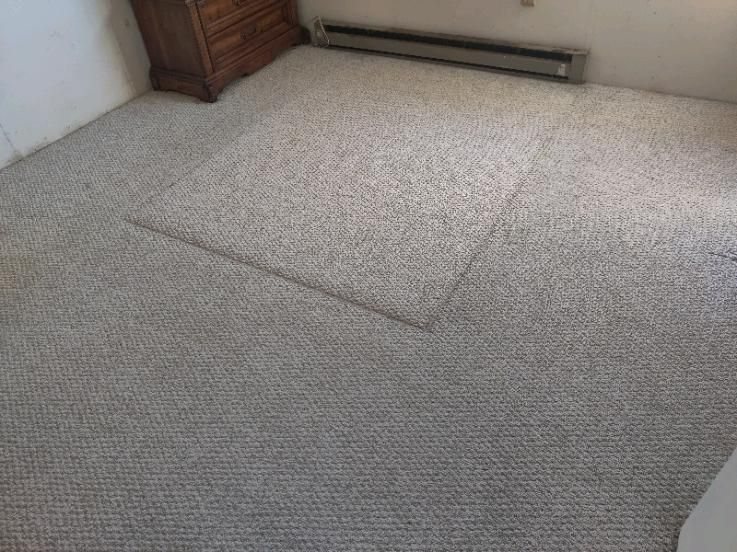 Beige carpeted room with a square cutout in the center. A wooden dresser is in the upper left corner.