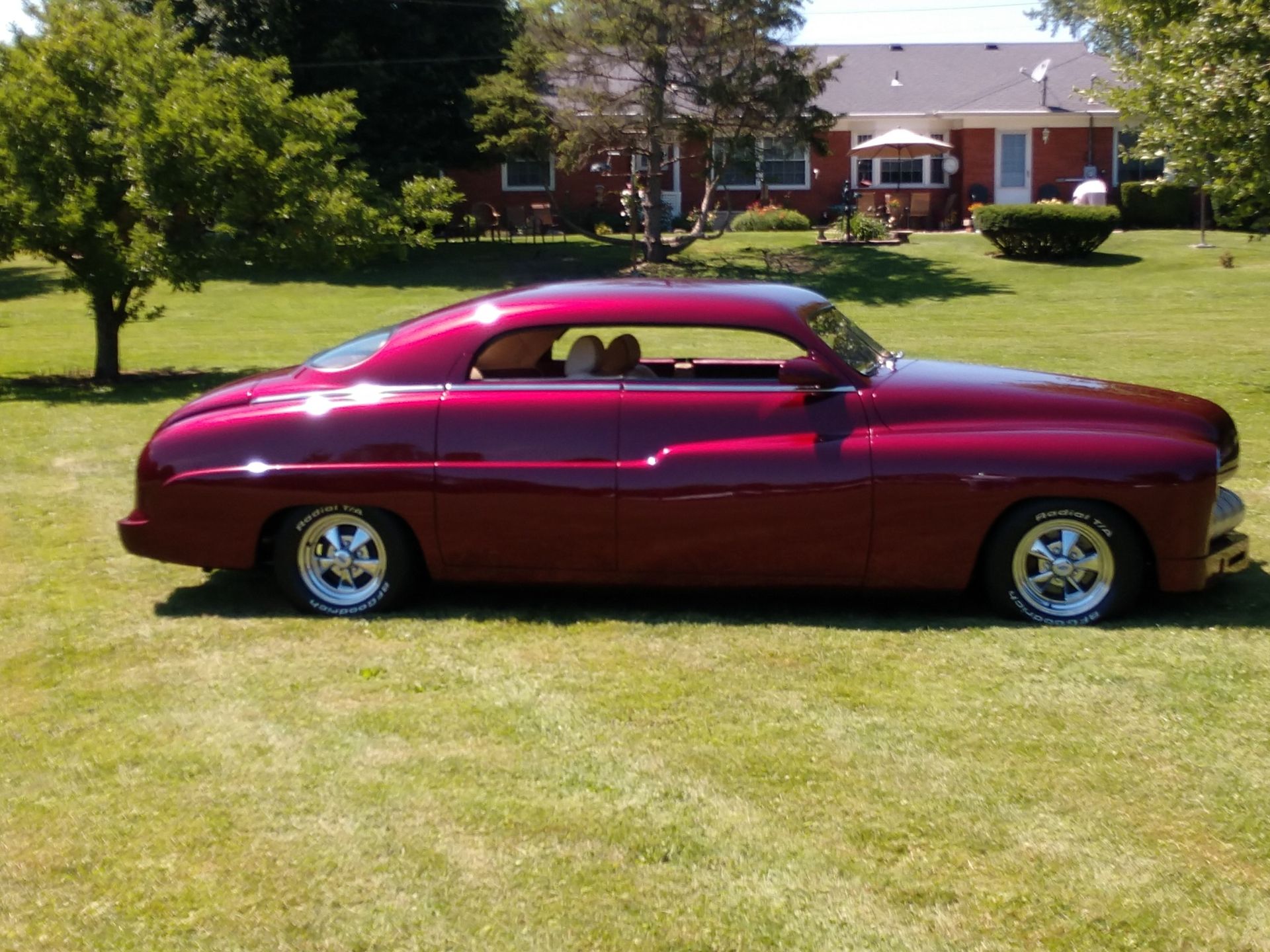 Classic maroon coupe parked on a grassy lawn in front of a house.