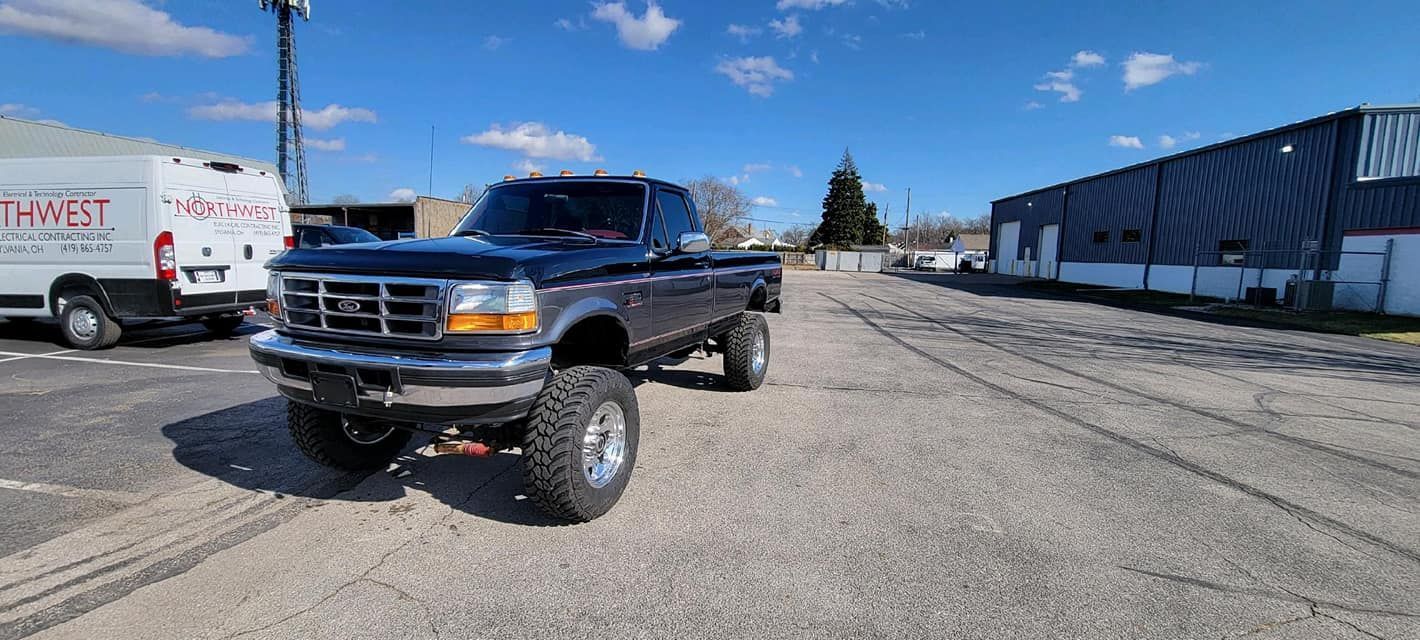 Lifted black pickup truck parked in an industrial lot on a sunny day