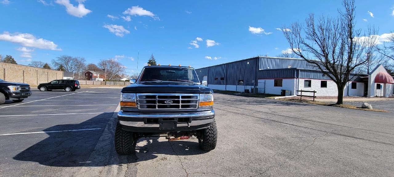 Front view of a black pickup truck parked in a mostly empty lot beside a long white building.