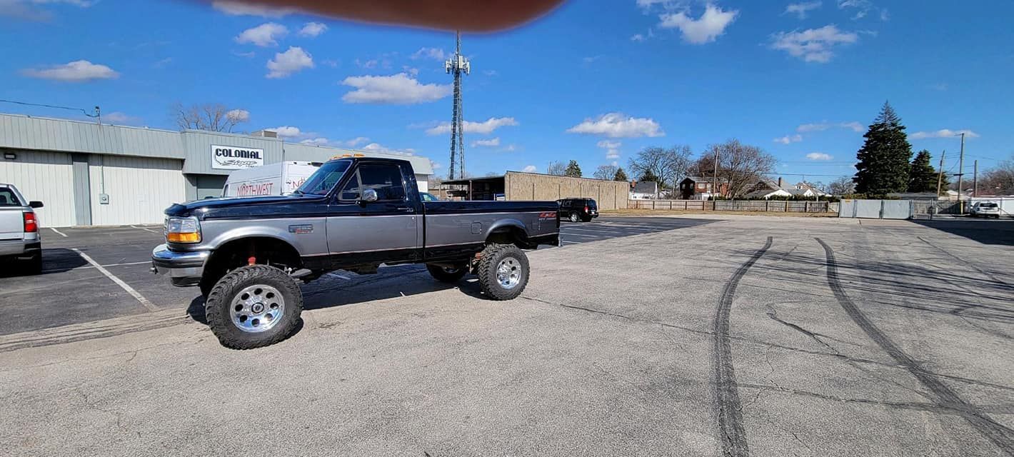 Lifted dark pickup truck parked in a lot under a clear blue sky.