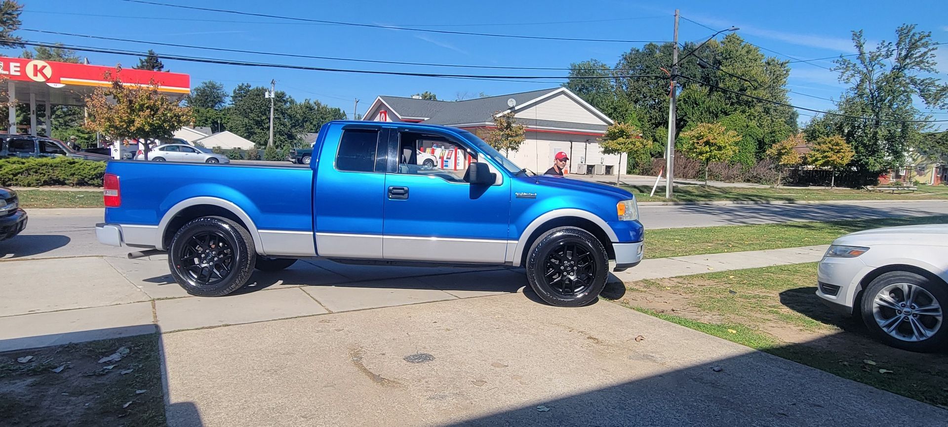 Blue pickup truck parked on a gravel lot beside a road on a sunny day.