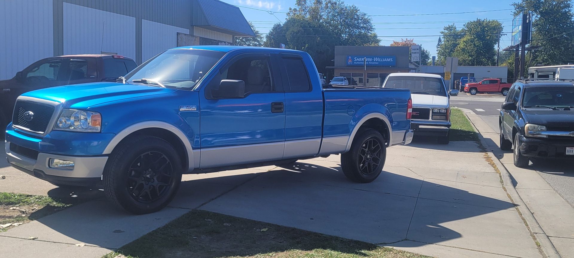 Blue lifted pickup truck parked on a sunny dealership lot, with other vehicles nearby.
