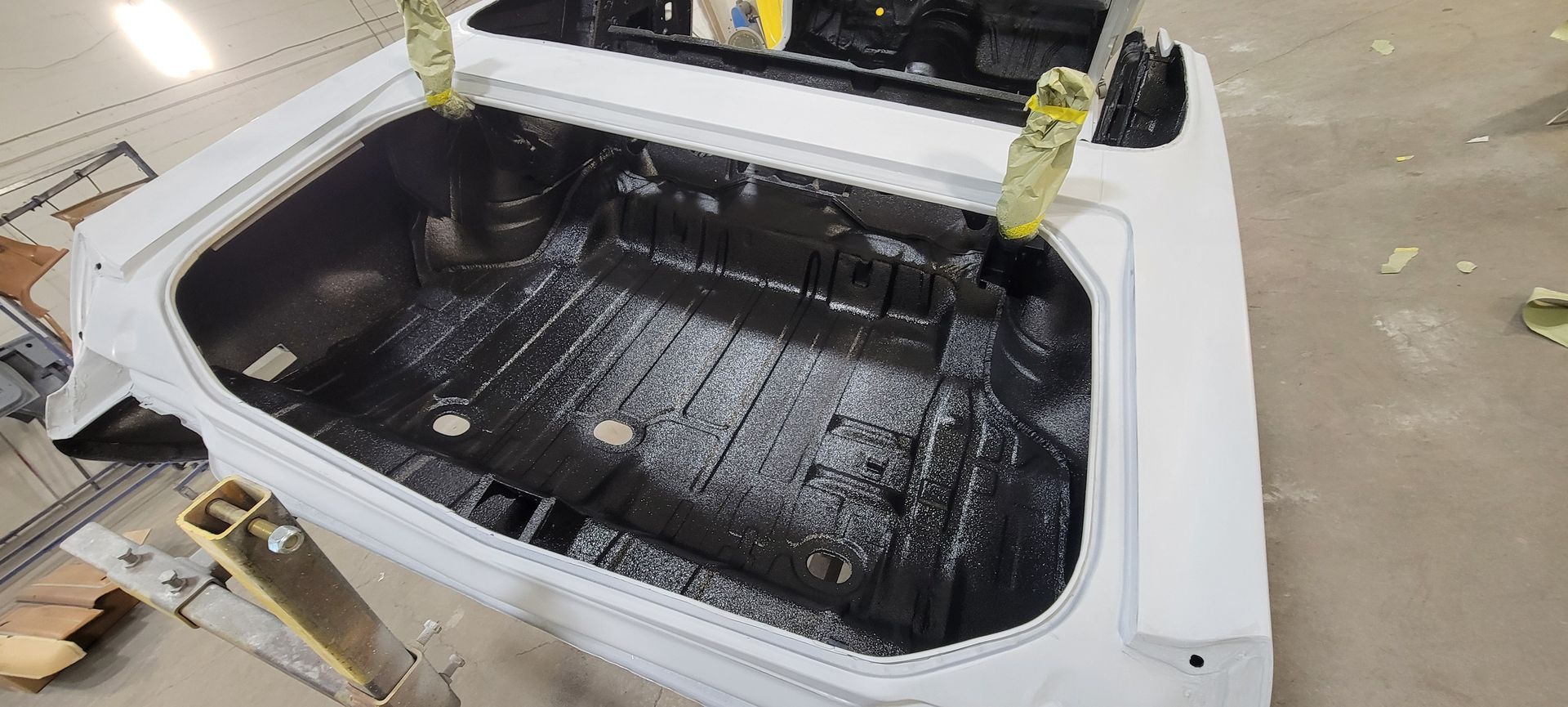 White pickup truck bed lined with a black spray-in coating, viewed from above in a garage.