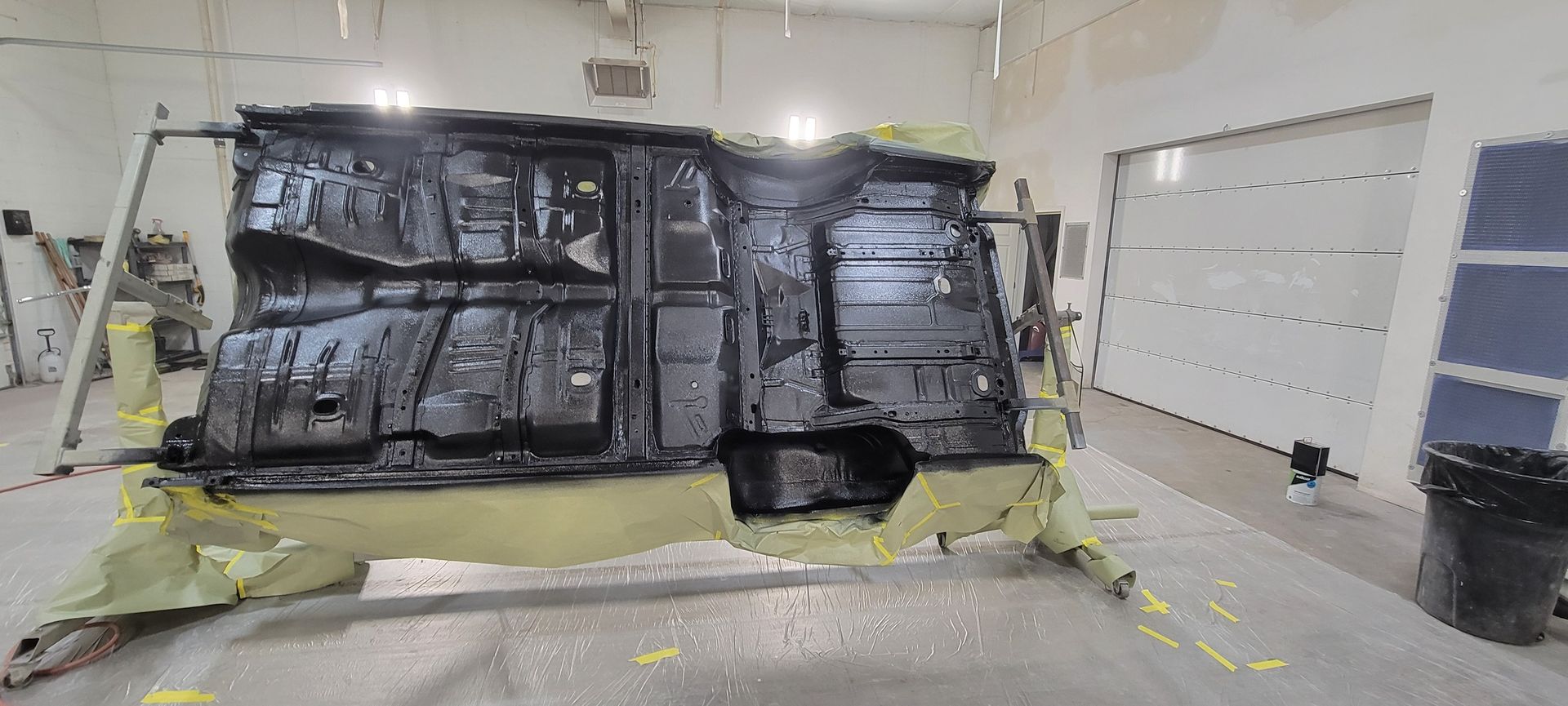 Large black tarp-covered structure in a bright room, with yellow tape and scattered equipment on the floor.