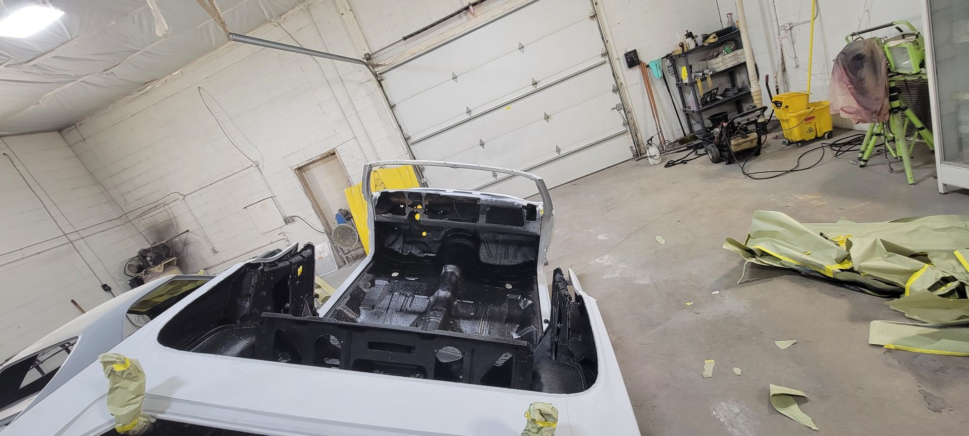 White car in a messy auto body shop with tools, equipment, and parts scattered around.