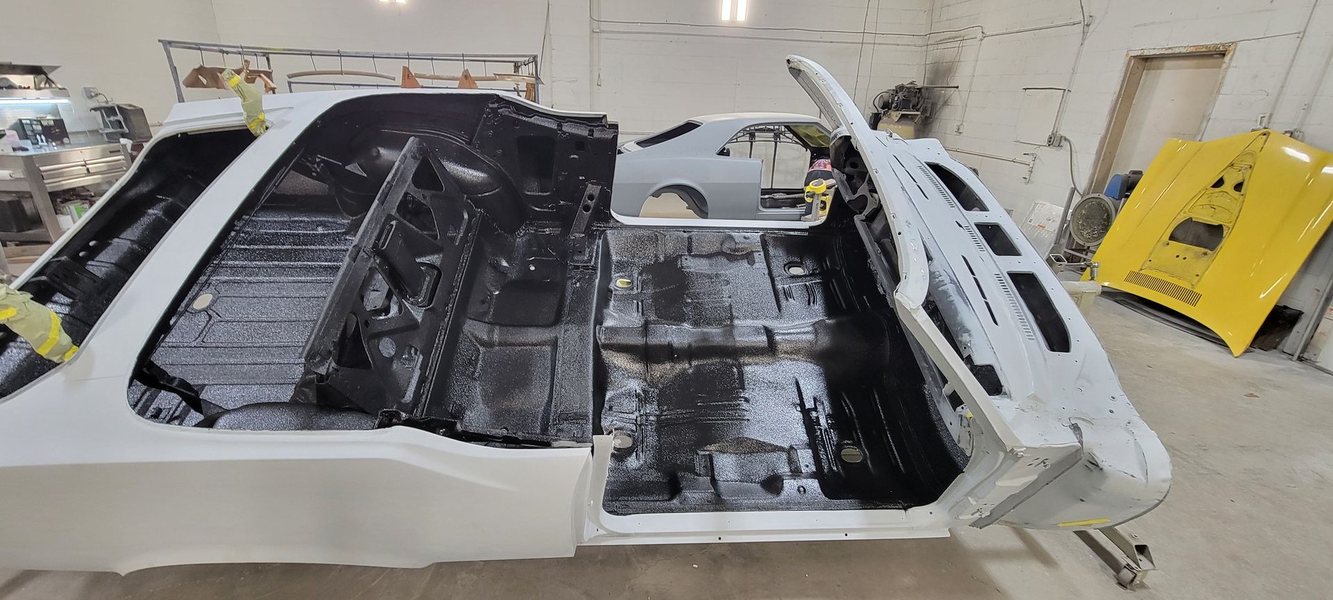 Severely burned car body shell in a workshop, with charred interior and detached panels
