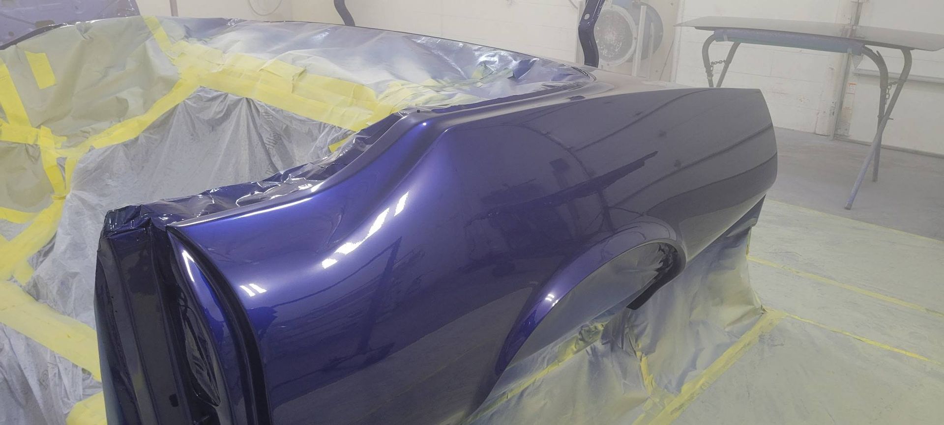 Glossy blue car body panel masked with plastic in a paint shop