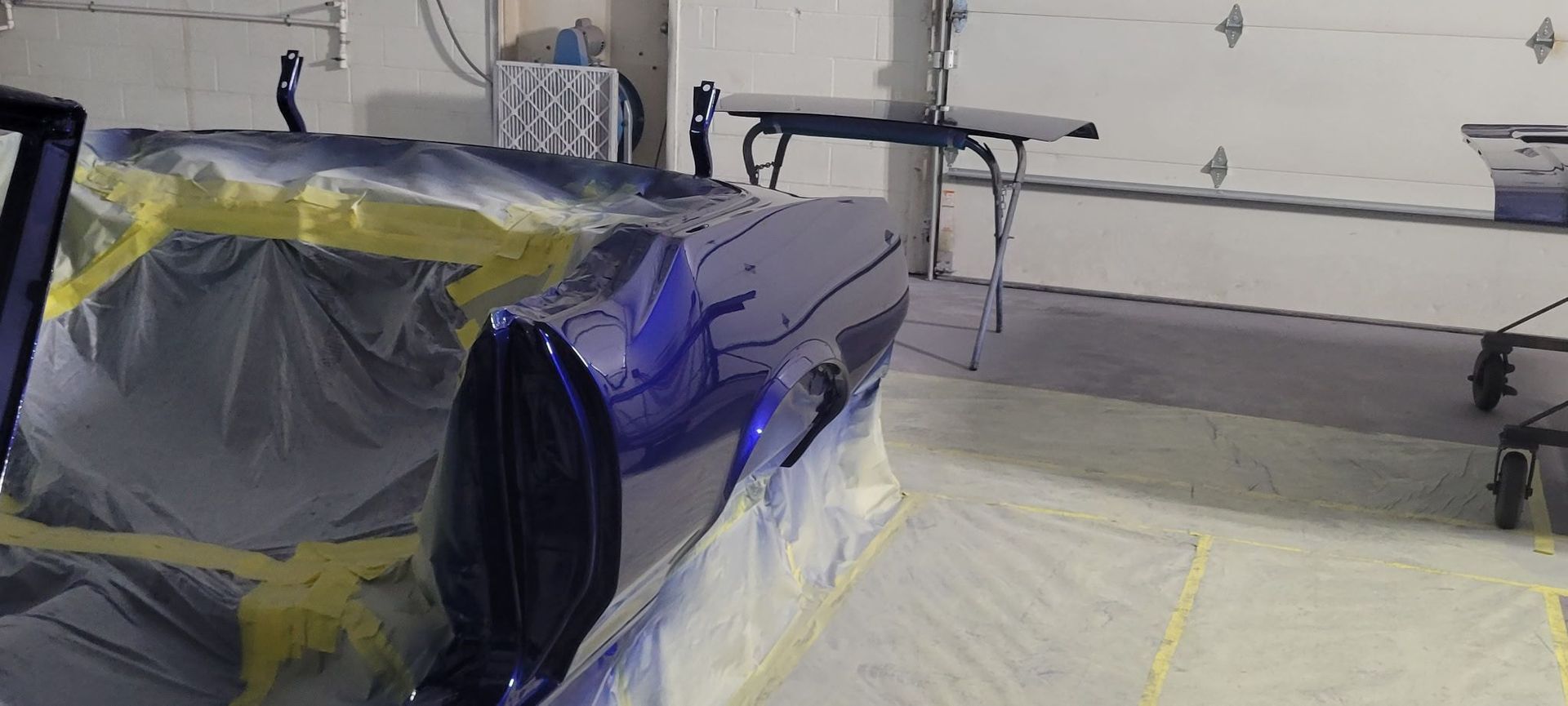 Car covered in plastic and tape inside a garage, with a work table in the background