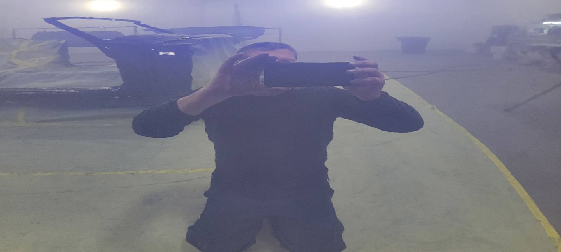Person taking a mirror selfie in a foggy room with a blue chair in the background.