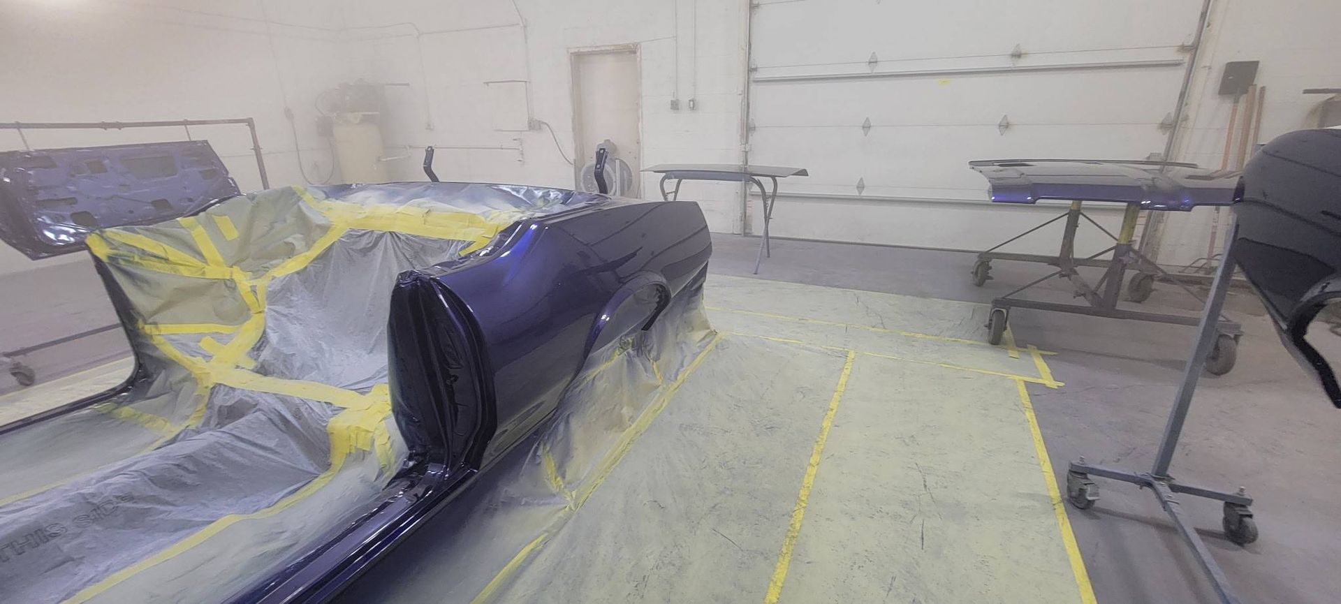 Garage with a car and furniture covered in plastic and taped off for painting or renovation.