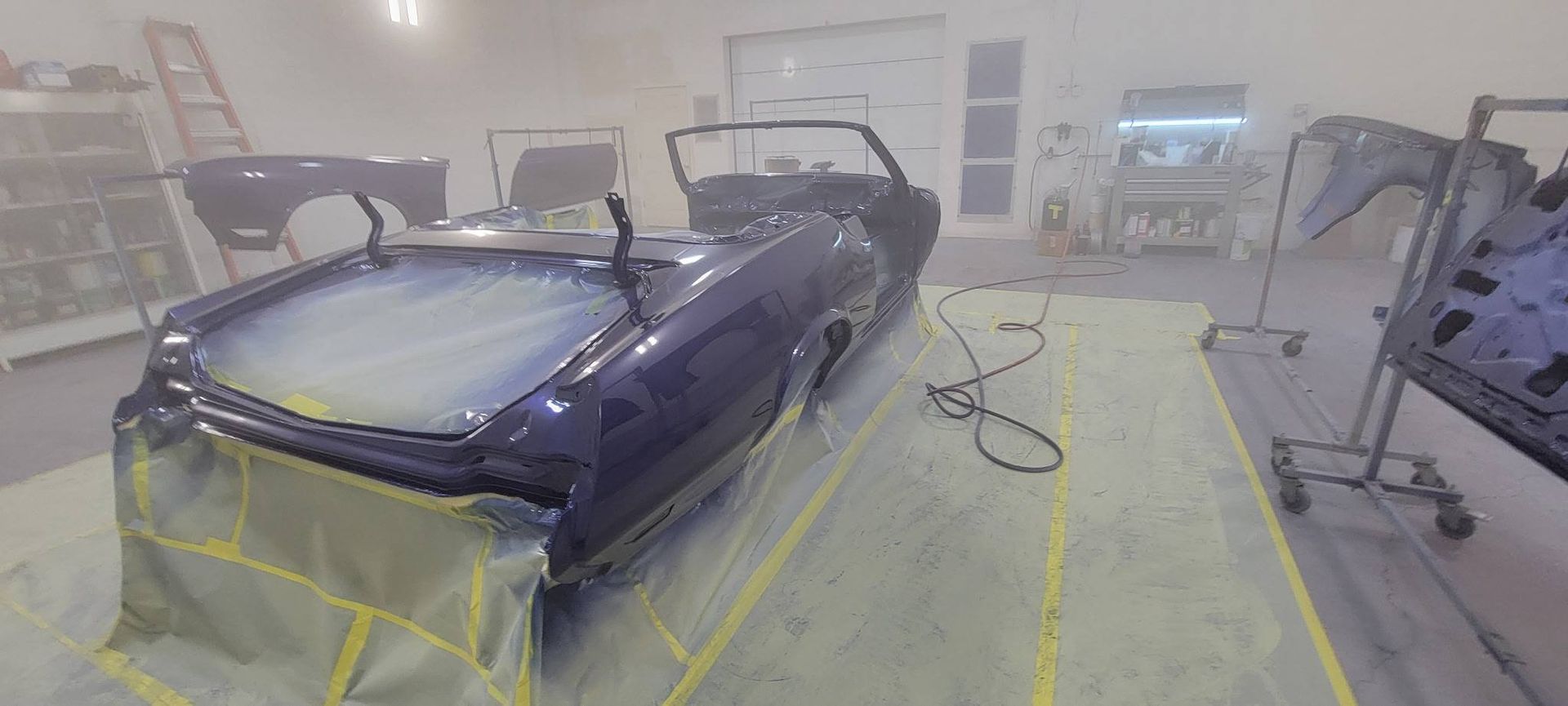 Blue convertible car masked and taped in an auto body paint booth